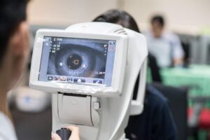An optometrist examines the eyes of an adult patient using specialized equipment in a bright exam room.